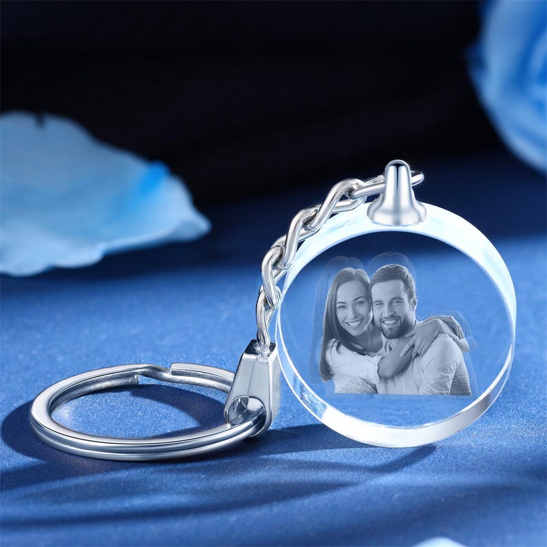 May include: A silver keychain with a clear crystal charm. The charm has a 3D engraved image of a couple embracing.