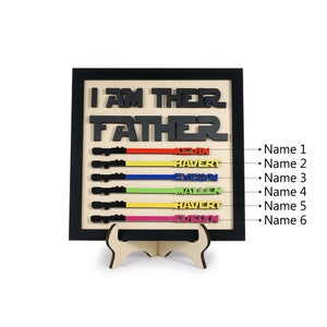 Puede incluir: Un letrero de madera con el texto "I am their Father" en letras negras. El letrero tiene seis ranuras en forma de sable de luz con rayas de colores y nombres escritos en ellas: Kevin, Havert, Even, Mallen, Havert, Evelyn.