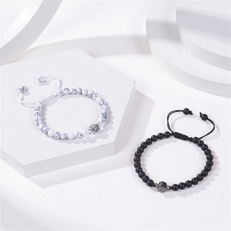 Pu&ograve; includere: Due braccialetti con perline, uno bianco con accenti neri e uno nero con accenti argentati. Entrambi i braccialetti hanno un ciondolo argentato al centro.