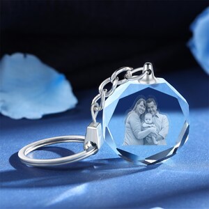 May include: A silver keychain with a clear crystal charm. The charm has a photo of a family of three inside. The photo shows a woman, a man, and a baby.