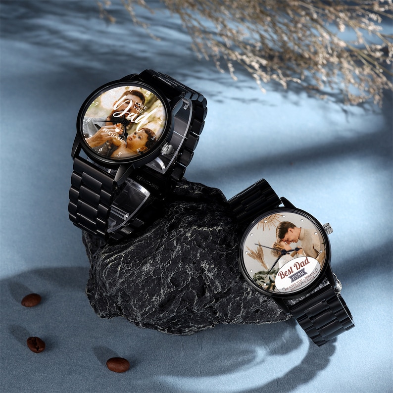 May include: Two black wristwatches with metal bands. The watch faces feature personalized photos and text. One watch says "I Love You Dad" and the other says "Best Dad Ever". The watches are displayed on a dark gray rock.