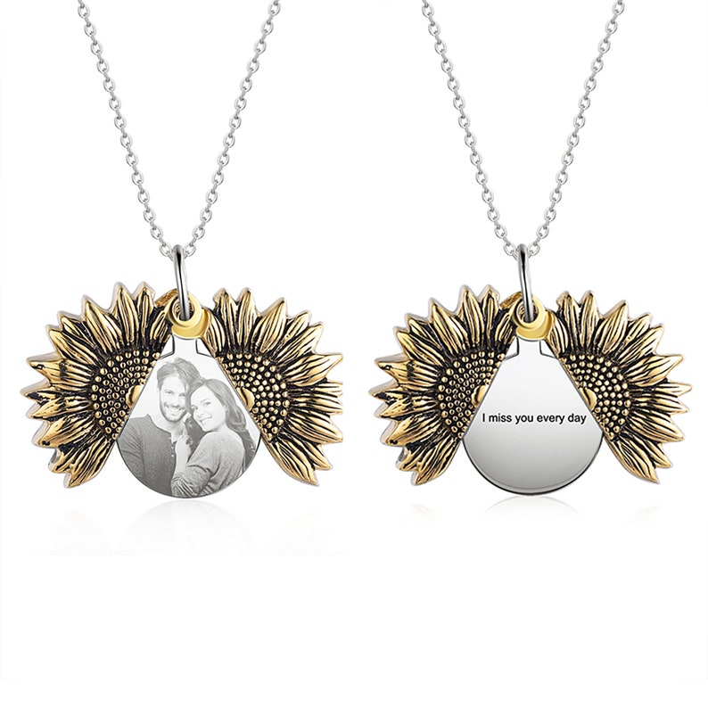 Pu&ograve; includere: Una collana d'argento con un ciondolo a forma di girasole. Il ciondolo si apre per rivelare una foto e la scritta "I miss you every day". Il girasole ha petali dorati e una catena d'argento.