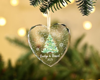 May include: A heart-shaped Christmas ornament with a watercolor Christmas tree design and the names "Evelyn & Daniel" and the year "2025." The ornament is clear with a white ribbon for hanging.