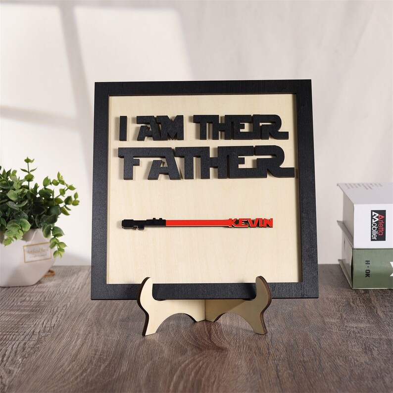 Puede incluir: Un letrero enmarcado de madera con el texto "I AM THEIR FATHER" en letras negras. El letrero tambi&eacute;n presenta un sable de luz rojo y el nombre "KEVIN" en letras negras.