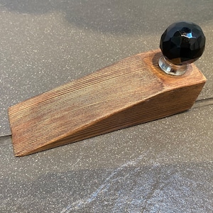May include: A wooden doorstop with a black glass knob. The doorstop is made of natural wood with a brown stain.