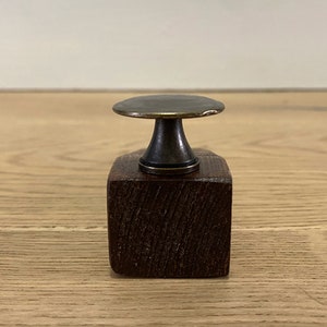 May include: A small, dark brown wooden base with a brass knob on top. The knob has a flat, circular top and a rounded, cylindrical base.