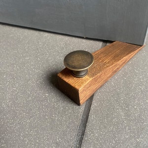 May include: A wooden doorstop with a brass knob. The doorstop is brown and has a natural wood finish. The knob is round and has a shiny finish.