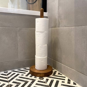 K&ouml;nnte beinhalten: Ein Toilettenpapierhalter aus Holz mit brauner Oberfl&auml;che und runder Basis. Der Halter ist mit vier Rollen wei&szlig;em Toilettenpapier gef&uuml;llt.