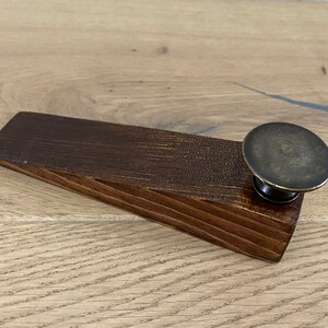 May include: A wooden doorstop with a dark brown stain and a brass knob on top.