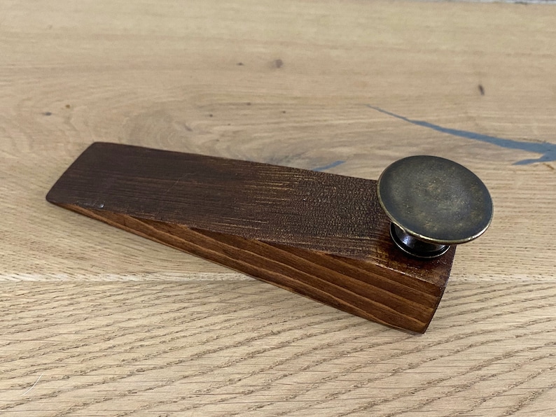 May include: A wooden doorstop with a dark brown stain and a brass knob on top.