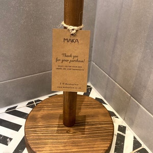 K&ouml;nnte beinhalten: Ein Holz-Papierrollenhalter mit braunem Sockel und braunem Stiel. Ein braunes Papieretikett ist mit einer Schnur am Stiel befestigt. Das Etikett lautet "MAKA PLACE" und "Vielen Dank f&uuml;r Ihren Kauf! Genie&szlig;en Sie 10 % Rabatt auf Ihre n&auml;chste Bestellung. Verwenden Sie den Code THANKYOU10 f@makaplace www.makaplace.co.uk"