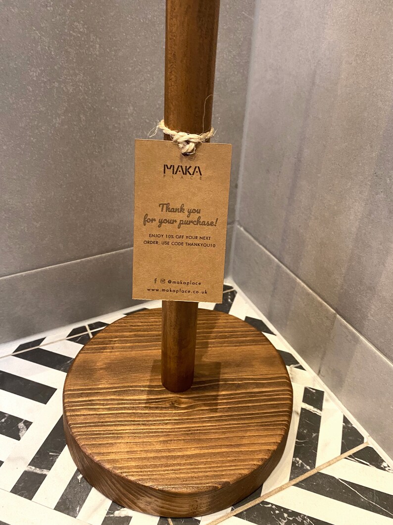 K&ouml;nnte beinhalten: Ein Holz-Papierrollenhalter mit braunem Sockel und braunem Stiel. Ein braunes Papieretikett ist mit einer Schnur am Stiel befestigt. Das Etikett lautet "MAKA PLACE" und "Vielen Dank f&uuml;r Ihren Kauf! Genie&szlig;en Sie 10 % Rabatt auf Ihre n&auml;chste Bestellung. Verwenden Sie den Code THANKYOU10 f@makaplace www.makaplace.co.uk"