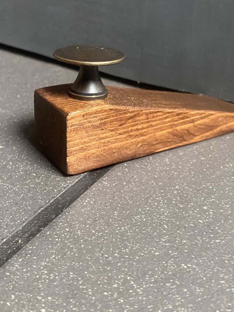 May include: A wooden doorstop with a dark brown stain and a brass knob on top.