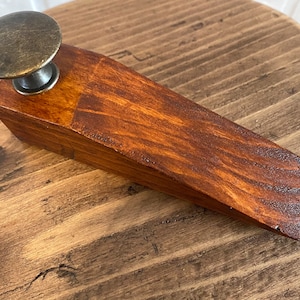 May include: A wooden doorstop with a dark brown stain and a brass knob on top.