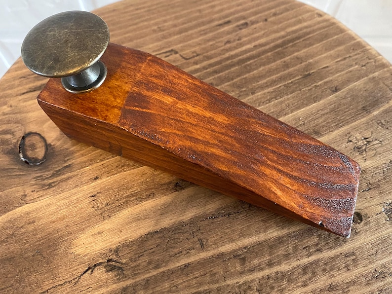 May include: A wooden doorstop with a dark brown stain and a brass knob on top.