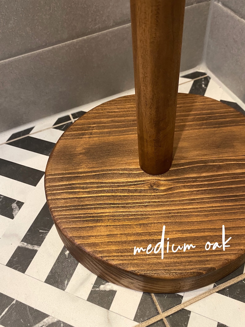K&ouml;nnte beinhalten: Ein Papierrollenhalter aus Holz mit einem runden Sockel. Der Sockel ist in einem mittleren Eichenholzton gebeizt und tr&auml;gt die Aufschrift "medium oak" in wei&szlig;er Farbe.