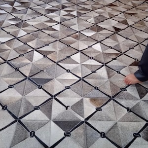 May include: A gray and white geometric patterned rug with black lines. The rug is made of leather and has a diamond pattern.
