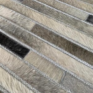 May include: A grey and white cowhide rug with a striped pattern. The rug is made of different pieces of cowhide sewn together.
