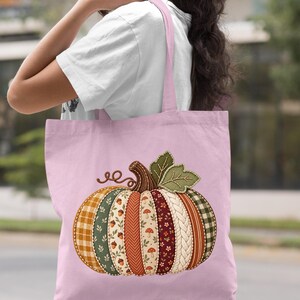 May include: A light pink tote bag featuring a large, central graphic of a pumpkin. The pumpkin is composed of vertical segments with various patterns, including plaid, floral, acorn, mushroom, herringbone, and cable knit textures in autumn colors.