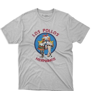 Peut inclure: T-shirt gris clair avec un dessin animé de deux poulets dans un cercle bleu, avec les mots "LOS POLLOS HERMANOS" en rouge. Le t-shirt a des manches courtes et un col rond.