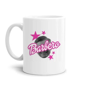 Puede incluir: Taza de cerámica blanca con una imagen en blanco y negro de una cara sonriente y el nombre "Barbero" en escritura rosa. Estrellas rosas rodean la imagen. La taza tiene un asa curva.