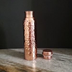Peut inclure: Une bouteille d'eau en cuivre martelé avec un couvercle assorti. La bouteille est de couleur cuivre clair et a une surface texturée.