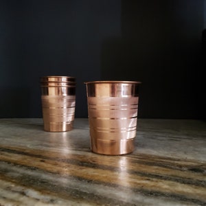 May include: Two copper drinking glasses with a hammered finish. The glasses are stacked on top of each other.
