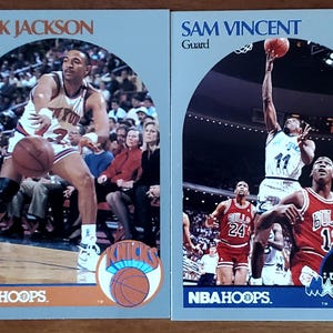 May include: Two vintage NBA Hoops basketball cards featuring Mark Jackson and Sam Vincent. Jackson is in a Knicks uniform, and Vincent is in a Hornets uniform. The cards have a blue and orange border with the NBA Hoops logo.