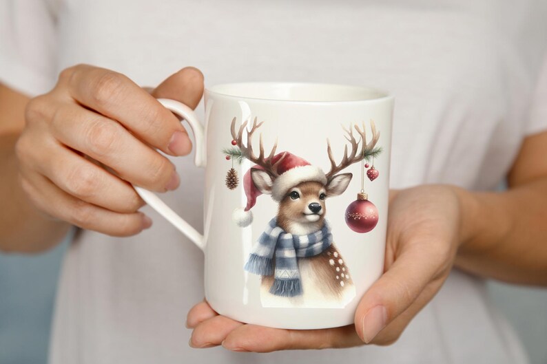 May include: White ceramic mug with a Christmas-themed design featuring a deer wearing a red Santa hat and a blue and white scarf. The deer has antlers with a pine branch and ornaments hanging from them.