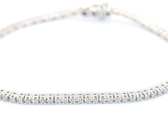 Puede incluir: Una delicada pulsera de plata con una fila de pequeños diamantes brillantes. La pulsera se muestra sobre un fondo blanco, resaltando el brillo de las piedras preciosas. El cierre es visible en la parte superior.