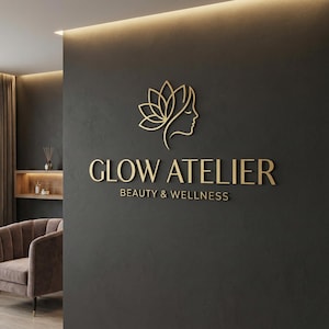 Könnte beinhalten: Goldenes Logo und Text auf einer dunkelgrauen Wand. Das Logo zeigt eine stilisierte Blume und ein Frauenprofil. Der Text lautet "GLOW ATELIER BEAUTY & WELLNESS". Ein brauner Sessel ist in der linken unteren Ecke zu sehen.