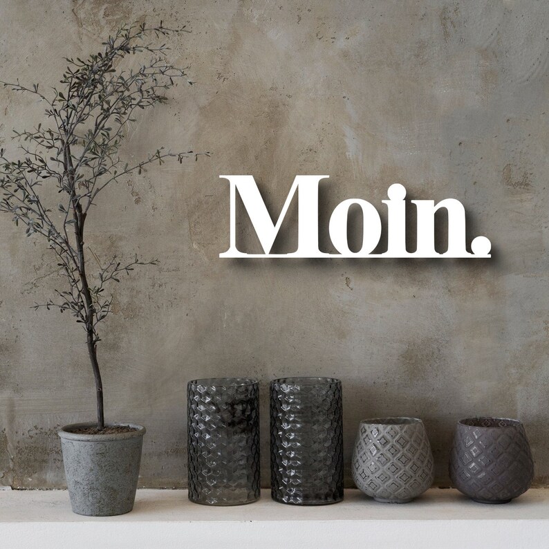 May include: White wooden sign with the word "Moin" on a gray textured wall. The sign is hanging above three gray textured cylindrical vases and two gray textured round vases.