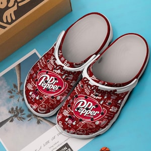 May include: Pair of red and white clogs with a Dr Pepper logo and various Dr Pepper-themed graphics. The clogs have a white interior and a red trim. The text "Dr Pepper Est. 1885" is visible.