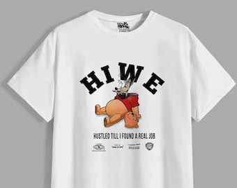 May include: A white short-sleeve t-shirt featuring a graphic of a cartoon bear wearing a red shirt, smoking, and reclining. Above the bear is the text HIWE in black, and below is the text HUSTLED TILL I FOUND A REAL JOB with small logos.