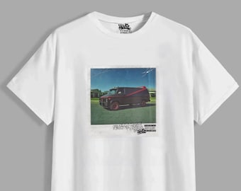 May include: A white short-sleeve t-shirt featuring a central graphic print of a dark van parked on a street, styled like a Polaroid photograph. The print includes text reading Good Kid, M.A.A.D City, A Film By Kendrick Lamar, and Parental Advisory.
