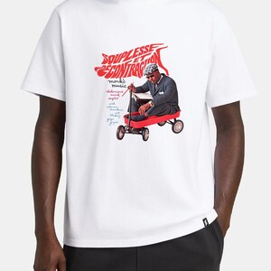 May include: A white short-sleeve t-shirt featuring a graphic print of a person in a suit and hat sitting in a red wagon. The text reads SOUPLESSE ET CONTRACTION, monk's music, thelonious monk, septet, with coleman hawkins, blakey, gigi gryce.