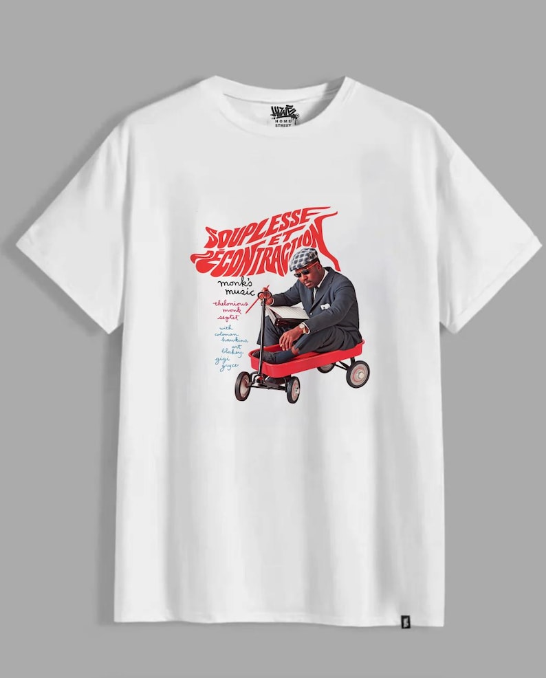 May include: A white short-sleeve t-shirt featuring a graphic of a person in a suit and hat sitting in a red wagon. The text reads "SOUPLESSE ET CONTRACTION" in red, along with "monk's music" and "thelonious monk septet" in smaller script.