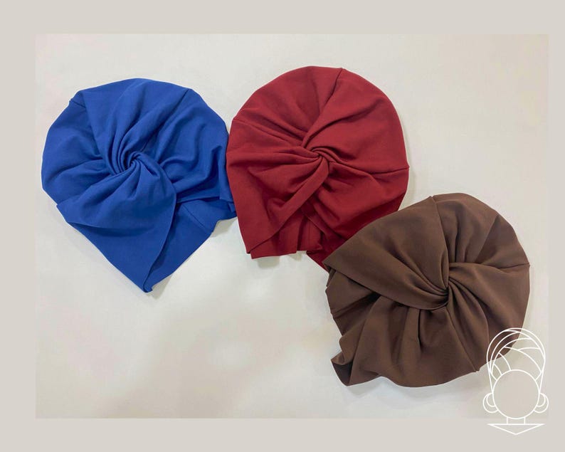 May include: Three turbans in solid colors: one bright blue, one deep burgundy red, and one dark brown. Each turban features a central twisted knot detail and gathered fabric construction, creating a soft, rounded shape with visible folds.