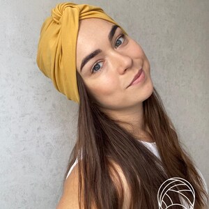 Pode incluir: Faixa de cabe&ccedil;a estilo turbante amarelo mostarda. O tecido &eacute; amarrado na parte superior, criando um acess&oacute;rio elegante e confort&aacute;vel. A faixa de cabe&ccedil;a &eacute; de cor s&oacute;lida e parece ser feita de um material macio. Esta faixa de cabe&ccedil;a &eacute; um &oacute;timo complemento para qualquer guarda-roupa.