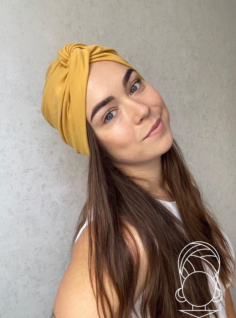 Pode incluir: Faixa de cabe&ccedil;a estilo turbante amarelo mostarda. O tecido &eacute; amarrado na parte superior, criando um acess&oacute;rio elegante e confort&aacute;vel. A faixa de cabe&ccedil;a &eacute; de cor s&oacute;lida e parece ser feita de um material macio. Esta faixa de cabe&ccedil;a &eacute; um &oacute;timo complemento para qualquer guarda-roupa.