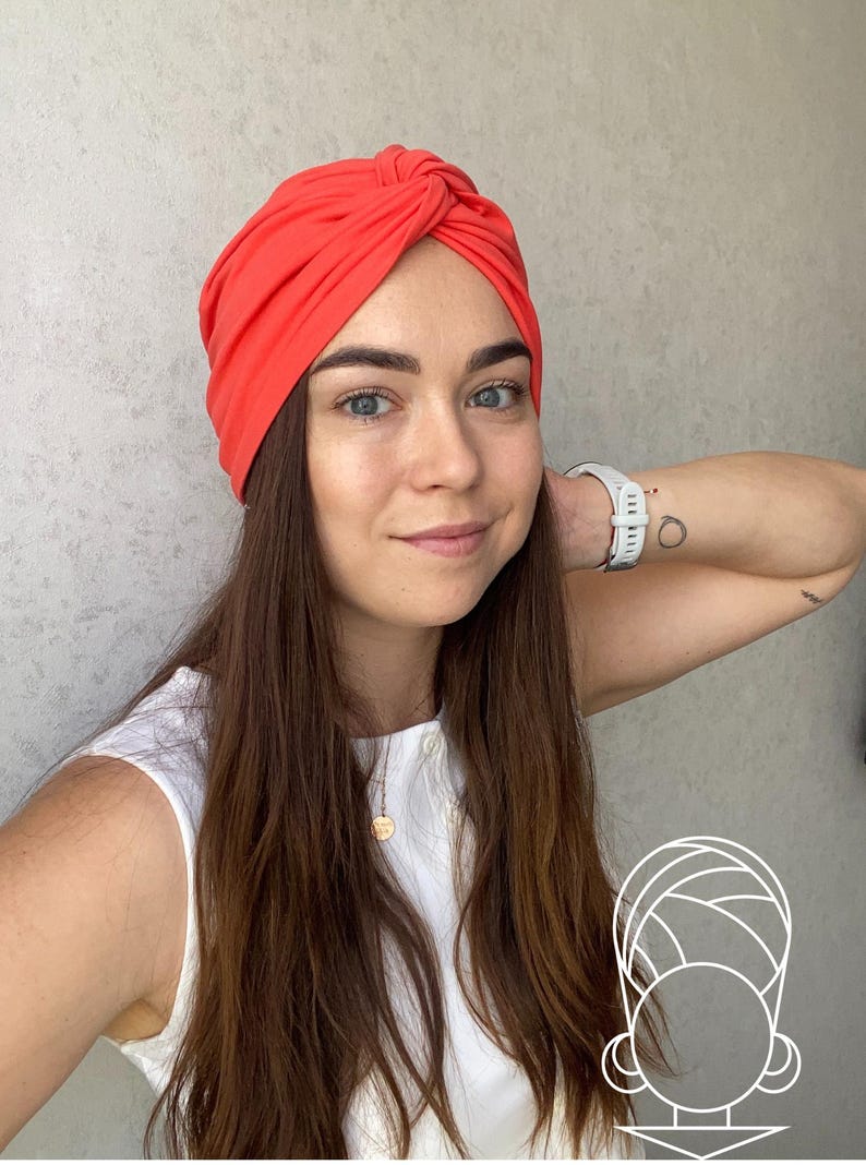 Pode incluir: Um turbante vibrante de cor coral. O adorno de cabe&ccedil;a &eacute; amarrado no topo e feito de um tecido macio. A mulher na imagem est&aacute; usando um top branco e um rel&oacute;gio branco.