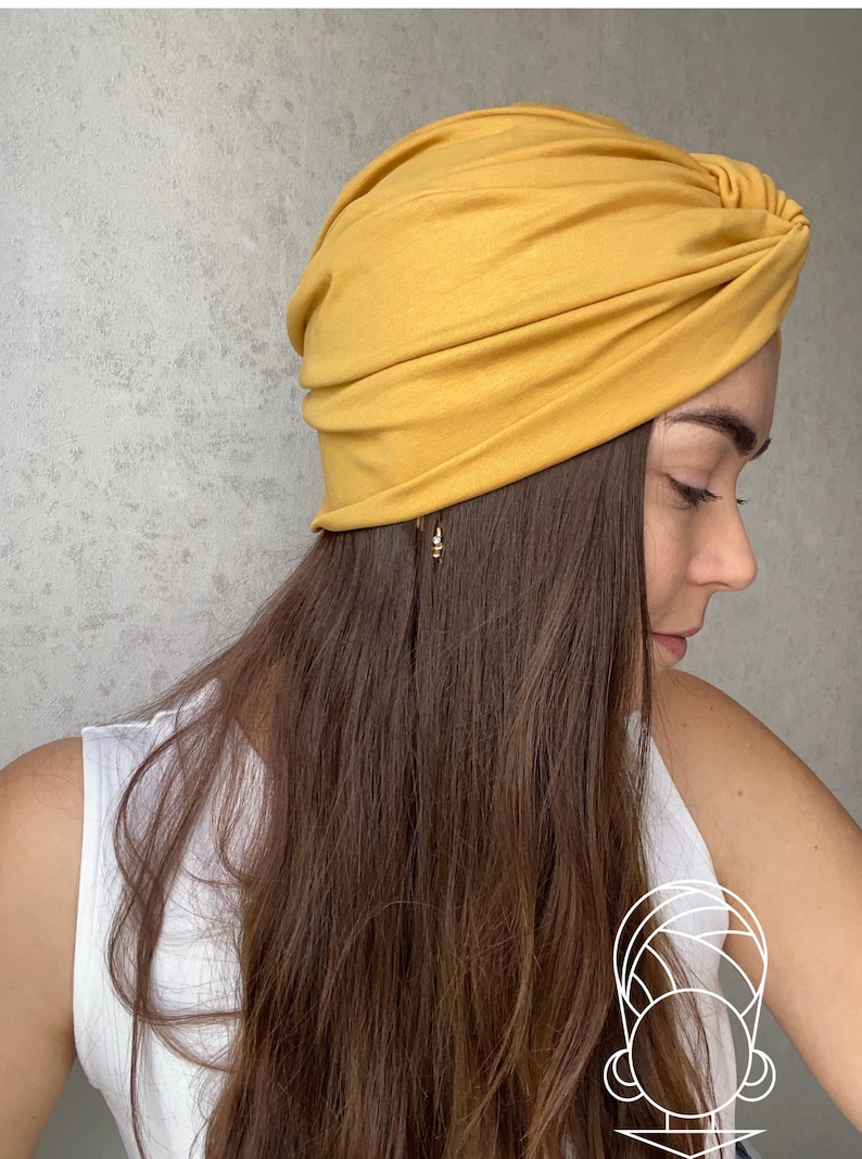 Pode incluir: Enrolamento de cabe&ccedil;a estilo turbante amarelo mostarda. O tecido &eacute; macio e franzido, com um detalhe de n&oacute; na parte superior. O adorno de cabe&ccedil;a &eacute; usado por uma pessoa com cabelo castanho comprido e uma regata branca.