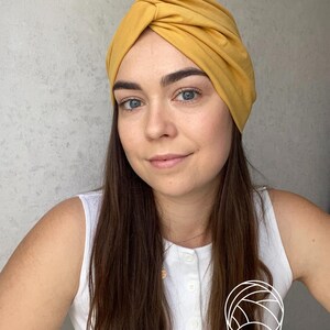 Pode incluir: Turbante amarelo mostarda. O tecido &eacute; franzido e torcido na parte superior, criando um acess&oacute;rio elegante e confort&aacute;vel. O turbante &eacute; de cor lisa e parece ser feito de um material macio. Este adere&ccedil;o de cabe&ccedil;a &eacute; adequado para v&aacute;rias ocasi&otilde;es.