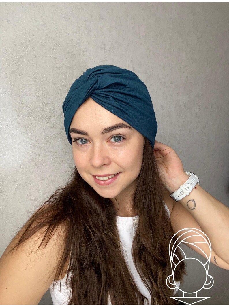 May include: A dark teal turban-style head wrap featuring a central twisted knot detail at the front. The fabric is smooth and fitted, covering the crown of the head securely. A small white line-art icon of a turban is visible in the corner.