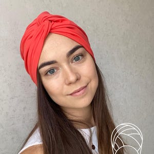 Pode incluir: Um turbante cor coral. O tecido &eacute; franzido e amarrado no topo, criando um acess&oacute;rio de cabe&ccedil;a elegante. Este acess&oacute;rio de cabe&ccedil;a &eacute; uma escolha elegante para v&aacute;rias ocasi&otilde;es.
