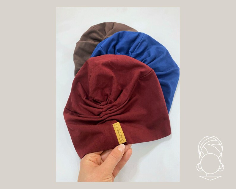 May include: Three soft fabric turbans in burgundy, royal blue, and brown. Each turban features a gathered, pleated design at the front and a small rectangular tan label with the text S'tarute B stitched onto the lower edge of the burgundy piece.