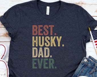 May include: A heather navy blue t-shirt with the text "BEST. HUSKY. DAD. EVER." in a vintage style font. The text is in yellow, orange, and green.