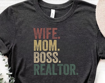 Könnte beinhalten: Ein dunkelgraues T-Shirt mit dem Text "WIFE. MOM. BOSS. REALTOR." in einer Vintage-Schriftart mit einem verblassten Regenbogen-Farbschema.