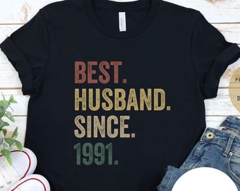 May include: Black t-shirt with a vintage-style graphic that reads "BEST. HUSBAND. SINCE. 1991."