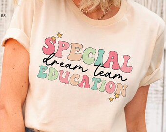 Pode incluir: Uma camiseta cor creme com o texto "SPECIAL dream team EDUCATION" em cores do arco-íris com estrelas de cada lado do texto.